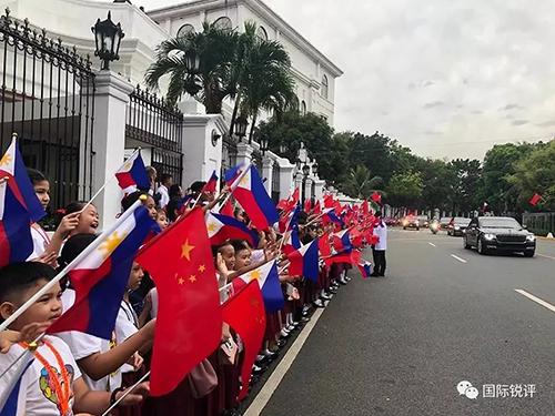 20日，来自马尼拉当地三所小学的千名小学生站在总统府道路两侧挥舞两国国旗，欢迎习主席车队。（图片来源：中央广播电视总台央视新闻 记者邓雪梅拍摄）